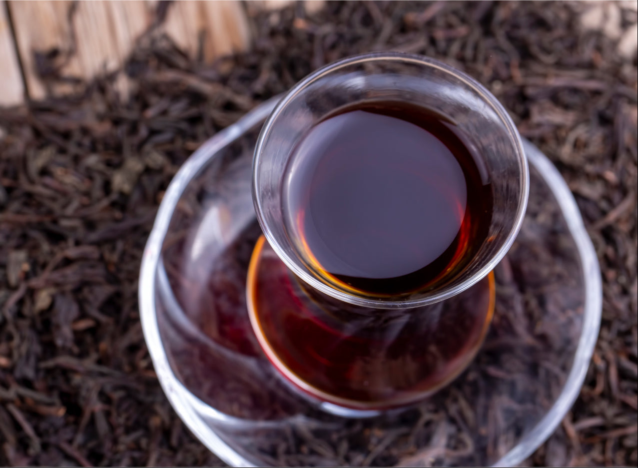 Glass cup of brewed black tea on a bed of loose black tea leaves