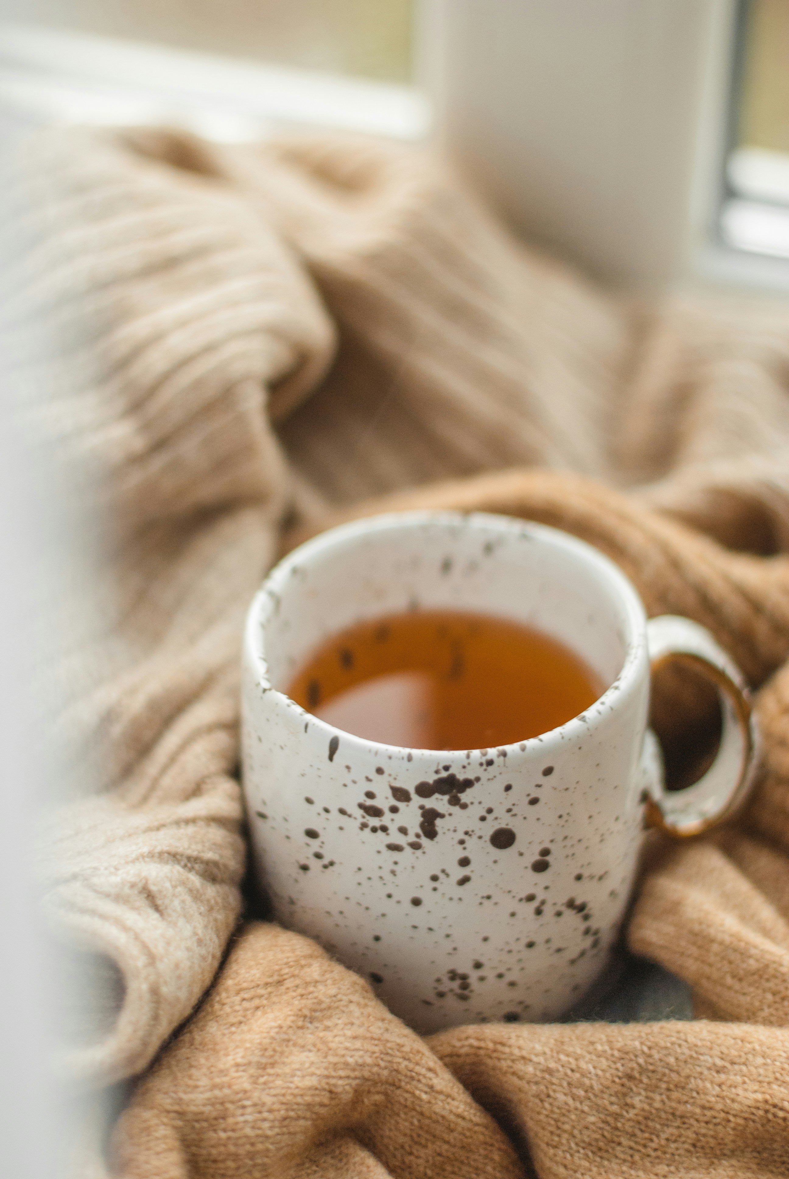 White speckled mug of tea nestled in a cosy beige blanket, lifestyle image for Krocus & Co. herbal tea