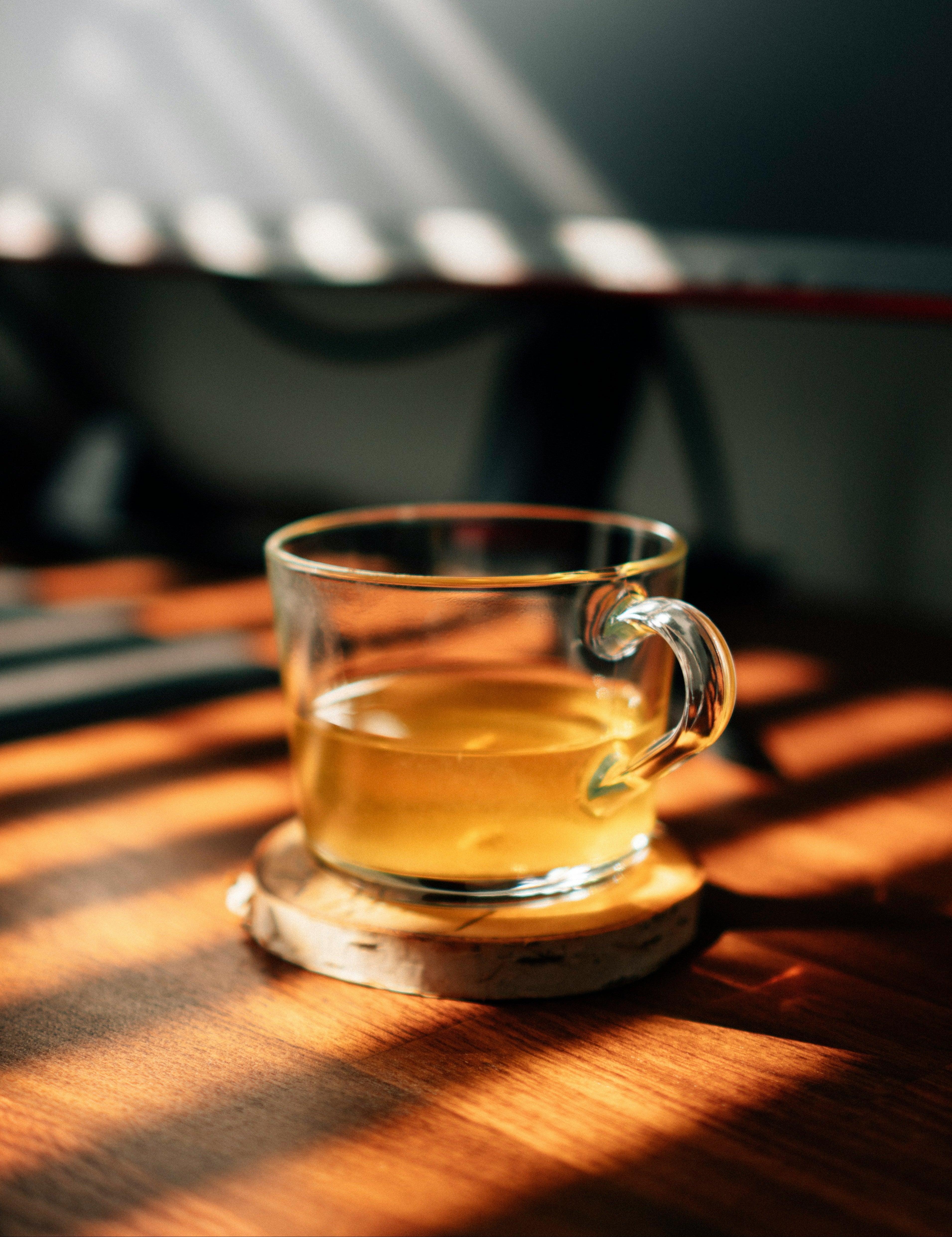 Glass tea cup with golden herbal tea on a wooden coaster with dramatic light and shadow
