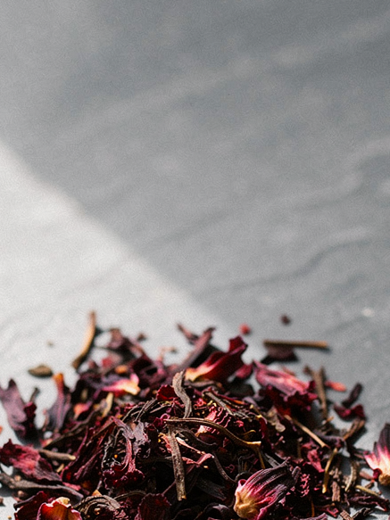 Dried hibiscus petals on a grey surface, an ingredient in Krocus & Co. Cinnamon & Clove herbal tea