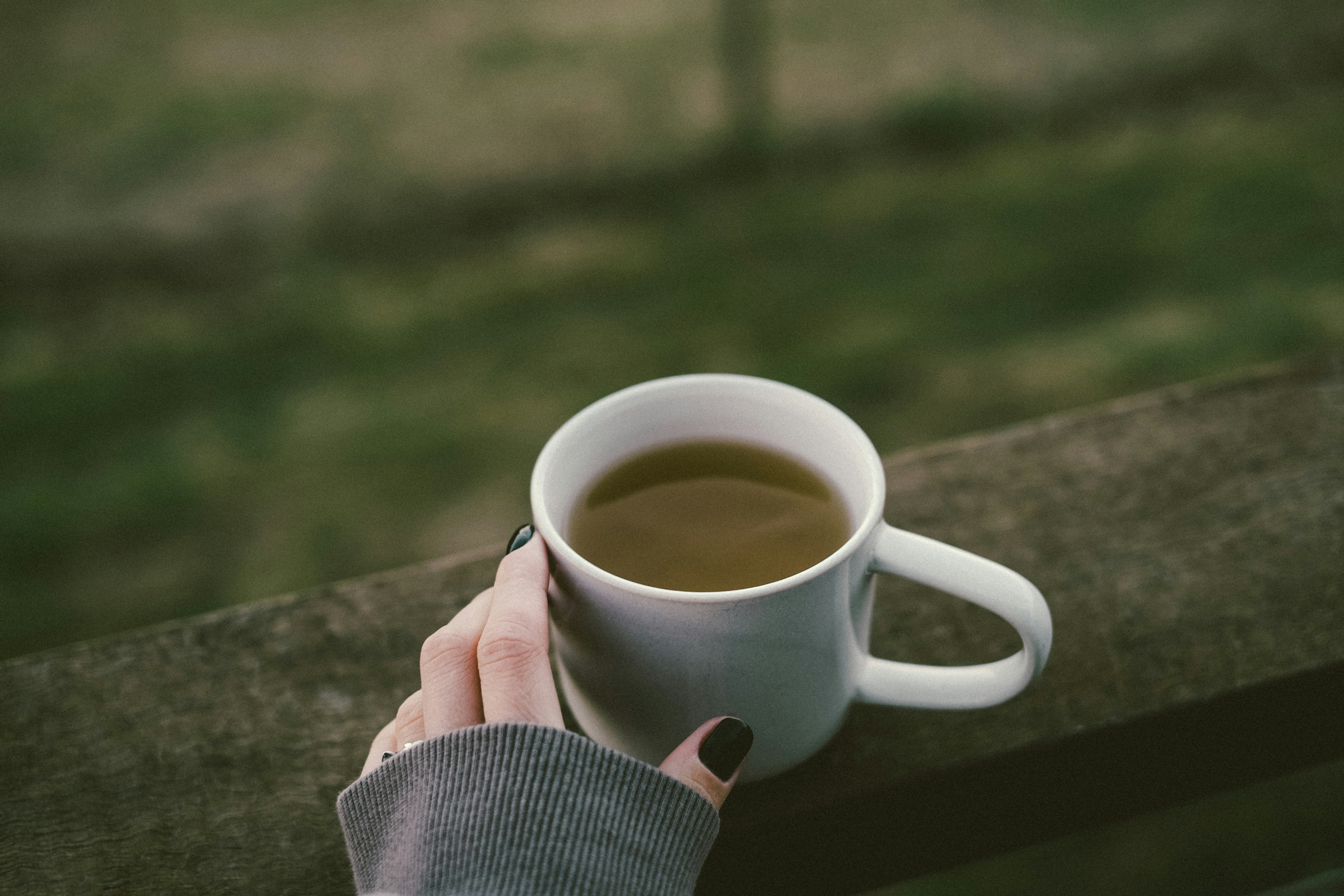 Hand holding a white mug of warm tea outdoors, lifestyle image for Krocus & Co. herbal tea